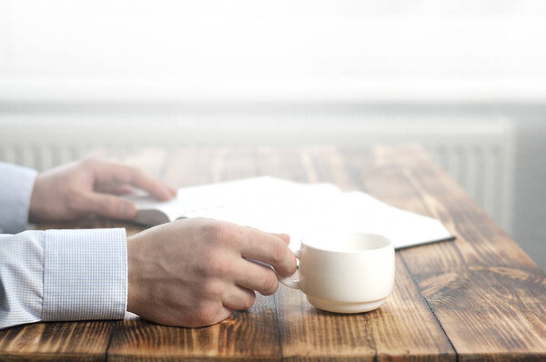 Откройте библейскую книгу и чашку кофе на деревянном столе. Руки молодого человека