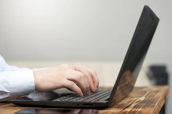 Open laptop and man\'s hands on a wooden table. Remote work. Freelancer workplace.