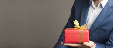 Bir iş adamı kırmızı bir paketin içinde fiyonklu bir hediye tutuyor. Sevgililer Günü. Aşk hediyesi.