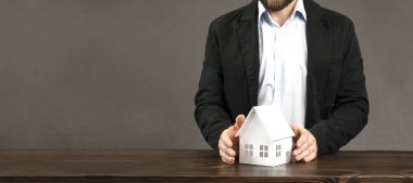 Erkek bir işadamının elinde bir evin minyatür tasarımı. Masanın üzerinde. Bir ölüye güvenlik ve koruma sağlama kavramı.