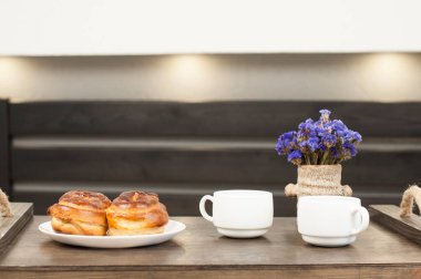 Tepside iki fincan kahve. Bir çörek ve bir buket çiçek. Yatakta kahvaltı..
