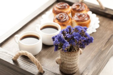 Tepside iki fincan kahve. Bir çörek ve bir buket çiçek. Yatakta kahvaltı..