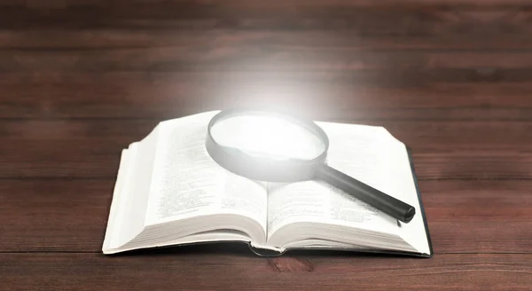Open Bible book on a wooden table. Holy Scripture. The sacred book. Magnifier