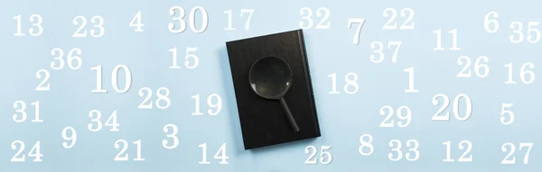 Closed black book and magnifying glass. On a blue background. The numbers are scattered in the background. Business robot. The concept of learning the alphabet, letters, writing, grammar, arithmetic, algebra, geometry