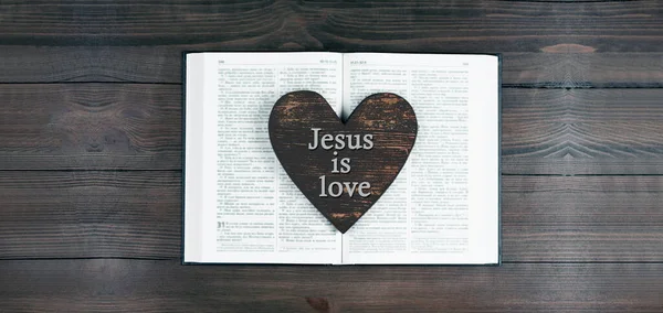 The open book is the holy bible. Scripture. Heart. Jesus is love. Prayer. On a wooden table.