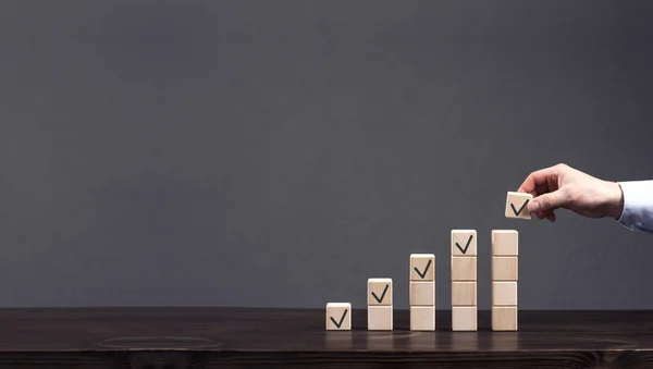 Wooden cubes are stacked in ascending order. The businessman\'s hand puts the top cube. Profit, finance growth concept. Progress