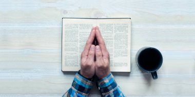 Açık İncil. Kutsal Kitap. Dua eden bir adamın elleri. Tahta bir masada.