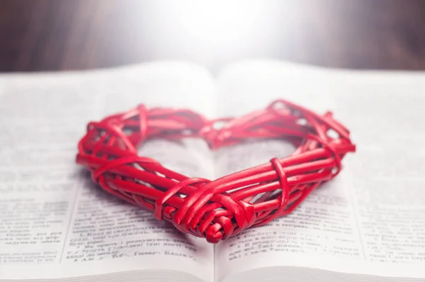 Open book Bible. Red heart on the book. Light beams. God love concept