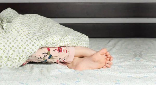 Bare feet of a child lying on the bed. Foot and toes. In the bed