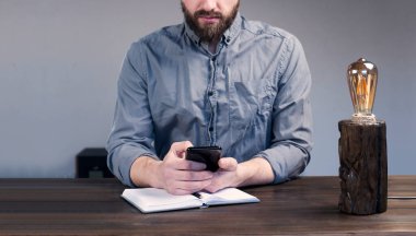 Elinde telefon olan genç bir iş adamı. Defteri aç. Masa lambası. Ahşap dekoratif lamba..