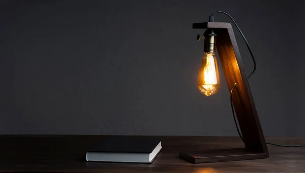 Table lamp and book notepad on the table. Wooden decorative lamp. Night light in the dark.