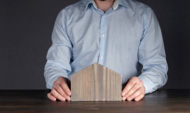 Gömlekli bir erkek işadamı. Evin minyatür bir modelini tutuyor. Küçük bir ev. Mülk koruma ve sigorta kavramı.