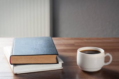 Ahşap bir masada iki kitap. Bir yığın kitap. Bir fincan kahve. İşyeri.