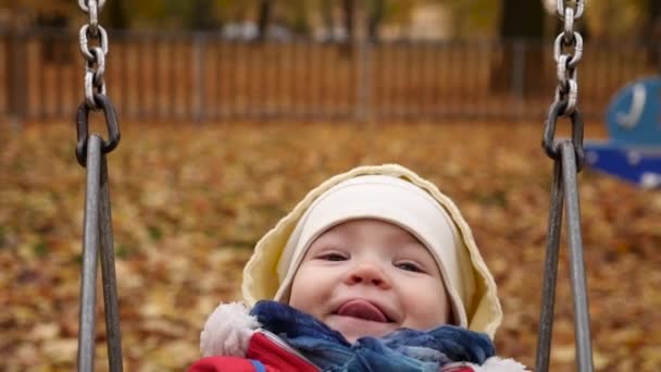 Happy baby på svingen i höst park framifrån slow motion — Stockvideo