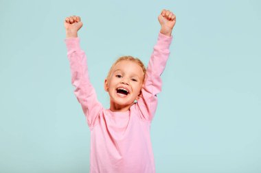 Mutlu gülümseyen, heyecanlı, pembe kazak giyen güzel bir kız. Mavi arka planda izole bir şekilde kameraya bakarak el ele tutuşun. Reklam için boş alan.