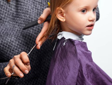 Saç kesme işlemi. Berber dükkanındaki güzel küçük kız, kuaför 4-5 yaşlarındaki şirin beyaz kıza saç stili yapıyor.