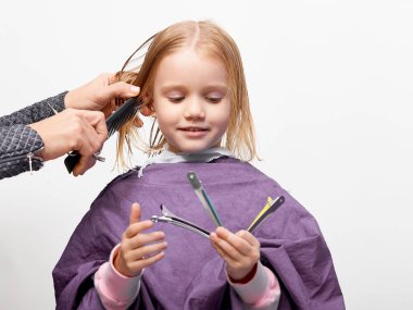 Saç kesme işlemi. Berber dükkanındaki güzel küçük kız, kuaför 4-5 yaşlarındaki şirin beyaz kıza saç stili yapıyor.