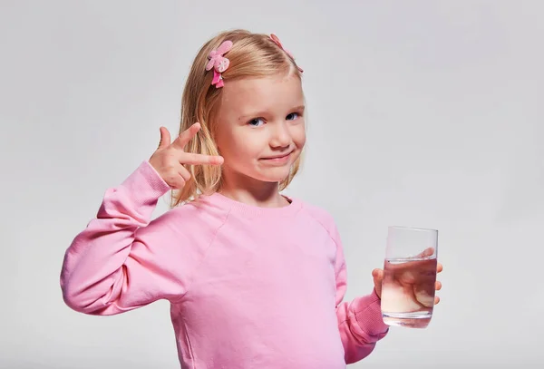 かわいい女の子の水のガラスを保持する 飲料水だ 肖像画のプロフィール 子供はガラスを手に持ってグレーの背景のカメラを見て — ストック写真