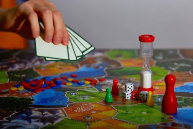 Senin hamlen - masa oyunu konsepti. Havada el ele oyun kartları var. Hamle yapıyor. Tahta oyun alanı, birçok şekil koyu bulanık arkaplan