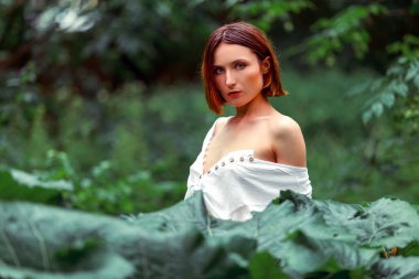 Beauty face woman bare shoulders behind green leaf plant. Portrait of caucasian woman's face surrounded by tropical leaves. Natural cosmetic, wellness, purity, skincare, beauty concept