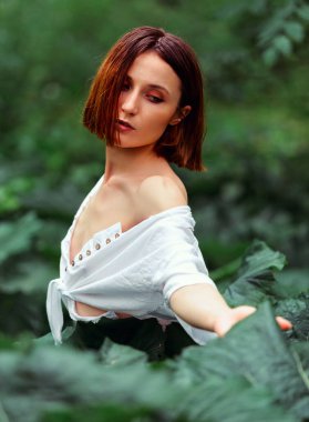 Beauty face woman bare shoulders behind green leaf plant. Portrait of caucasian woman's face surrounded by tropical leaves. Natural cosmetic, wellness, purity, skincare, beauty concept