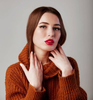 Balıkçı yaka kazaklı, yaka kazaklı genç ve güzel bir kadın. Kırmızı dudaklı sevimli bir kadın model. Stüdyoda, gri arka planda.