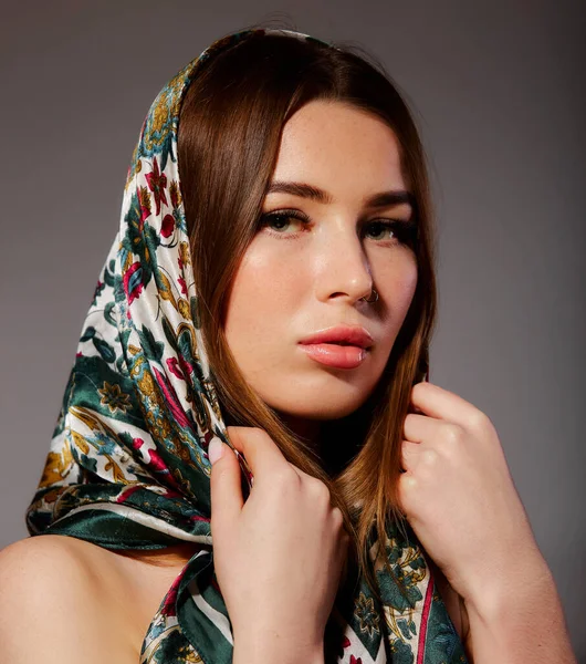 Portrait of a young woman with bright makeup and a fashionable headscarf. Gray background. Beauty, fashion, makeup concept.