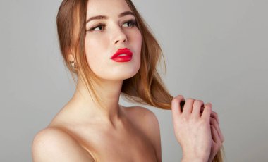 Uzun, sağlıklı düz saçlar. Uzun, kahverengi saçlı, kırmızı dudaklı ve burnu piercingli güzel bir kadın. Gri bir arkaplanda izole edilmiş esmer model portresi.