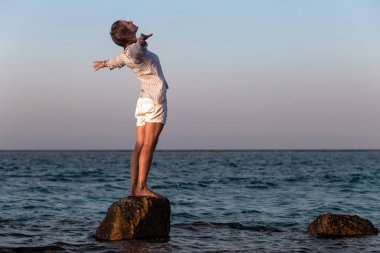 Özgürlüğün tadını çıkaran kadın. Kollarını arkaya uzat ve güneşli gökyüzünün altında denizin sahilinde hayatın tadını çıkar..