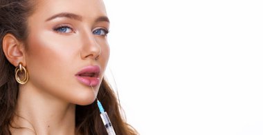 Güzel bir kadın beyaz arka planda dudaklarını büyütmek için iğne yapıyor. Mavi gözlü esmerin güzel portresi. Yüz bakımı, yüz bakımı, kozmetik konsept güzellik ve sağlıklı cilt.