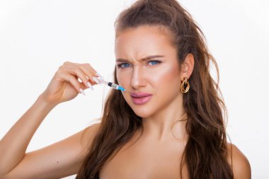 Güzel bir kadın beyaz arka planda dudaklarını büyütmek için iğne yapıyor. Mavi gözlü esmerin güzel portresi. Yüz bakımı, yüz bakımı, kozmetik konsept güzellik ve sağlıklı cilt.