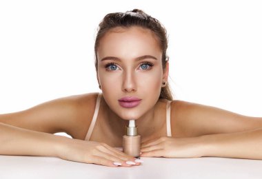 Masada oturan zarif ve neşeli bir kadın vakıf ya da cilt bakımı ürünü bulundurur. Mavi gözlü, bronzlaşmış tenli çekici bir kadın. Beyazda izole edilmiş fotokopi çekilen kameraya bakıyor.