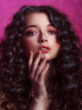Uzun, parlak dalgalı saçlı esmer kadın. Kıvırcık saçlı güzel bir yüz modeli. Pembe neon arka planda elleri Fransız manikürü olan bir kadın.