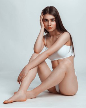 Beyaz iç çamaşırlarıyla poz veren güzel, baştan çıkarıcı bir kadın. Gri arka planda sportif bir figür. Seksi beyaz iç çamaşırlı zayıf bir kadın..