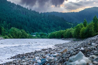 Gün batımında dağlara doğru uzanan kayalıklı berrak bir nehir.
