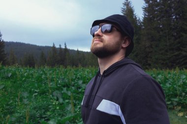 Güneş gözlüklü ve örgü şapkalı yakışıklı ve ciddi bir adam dağ yolculuğunun keyfini çıkarıyor.