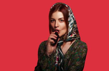 Burnunda piercing olan ve başörtüsü olan elektronik sigara içen bir kadın. Kırmızı arkaplan, metin için boşluk. Güzellik, moda konsepti.