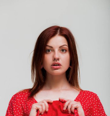 Yüz ifadesi. Şaşkın gözlerle ve delinmiş burunla etek tutan bir kadın. Gri arkaplan, kopyalama alanı. Metin için kadın yüzü delici boşluk