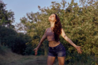 Parkta yaz güneşinin tadını çıkaran güzel bir kadın. Altın saatinde kotlar ve bej bluzlar.