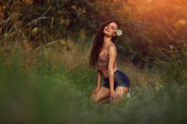 Gün batımının çim ışınlarında tarlada poz veren seksi kadın. Doğada yaşam tarzı kot şort ve bej bluz giyerek altın saat. Romantik sonbahar havası, çayırda uzun otlar.