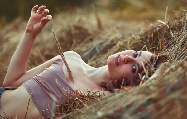 美丽性感的年轻女子躺在夕阳西下的干草中 穿着牛仔裤短裤和米黄色上衣 过着自然的生活 浪漫的秋天心情 黄金时刻 — 图库照片