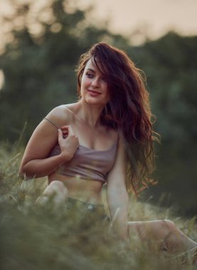 Gün batımında samanlıkta poz veren güzel seksi genç bir kadın. Kot şort ve bej bluz giymiş, doğada bir yaşam tarzı var. Romantik sonbahar havası, altın saat