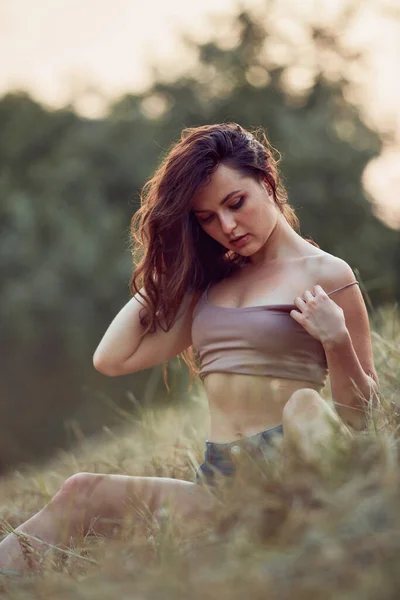 美丽性感的年轻女子躺在夕阳西下的干草中 穿着牛仔裤短裤和米黄色上衣 过着自然的生活 浪漫的秋天心情 黄金时刻 — 图库照片