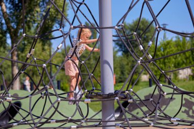 Aktif sarışın kız yaz mevsiminde oyun alanında iplere tırmanmaktan mutluluk duyar.