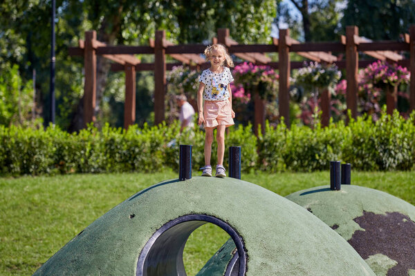 Active blonde girl play on obstacle course in playground in summer time