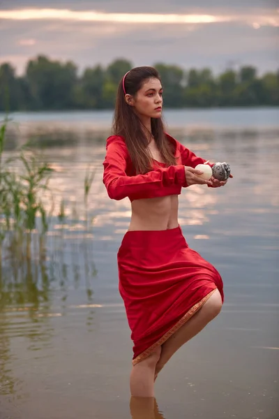 Ritual dance with candles in hands. Brunette woman in red costume for belly-dance is dancing on the beach