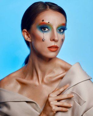 Moda yaratıcı makyaj. Temiz ve parlak ciltli genç bir kadının güzel portresi ve parlak mavi bir arka planda duran yapay elmaslarla süslenmiş.