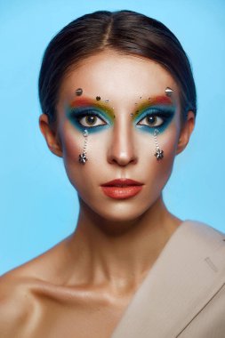 Moda yaratıcı makyaj. Temiz ve parlak ciltli genç bir kadının güzel portresi ve parlak mavi bir arka planda duran yapay elmaslarla süslenmiş.