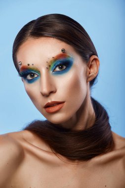 Moda yaratıcı makyaj. Temiz ve parlak ciltli genç bir kadının güzel portresi ve parlak mavi bir arka planda duran yapay elmaslarla süslenmiş.