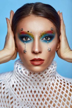 Moda yaratıcı makyaj. Temiz ve parlak ciltli genç bir kadının güzel portresi ve parlak mavi bir arka planda duran yapay elmaslarla süslenmiş.